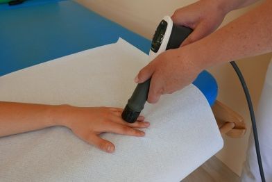 Urządzenie do terapii falą uderzeniową wyposażone jest w aplikator fali. Na zdjęciu - aplikator dotyka dłoni pacjenta.