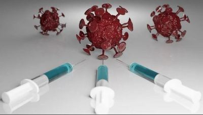 Informację o szczepieniach ilustruje graficzny symbol wirusa COVID, w którego wycelowane są igły strzykawek. 